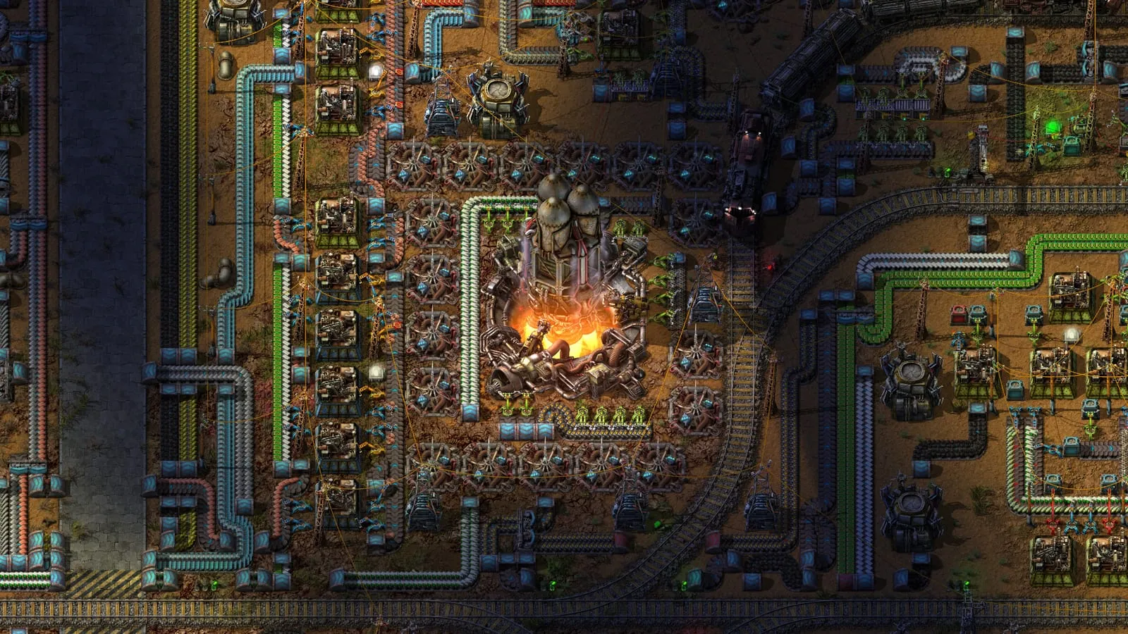Factorio – pohled shora na továrnu s rafinérií, potrubím a železnicí