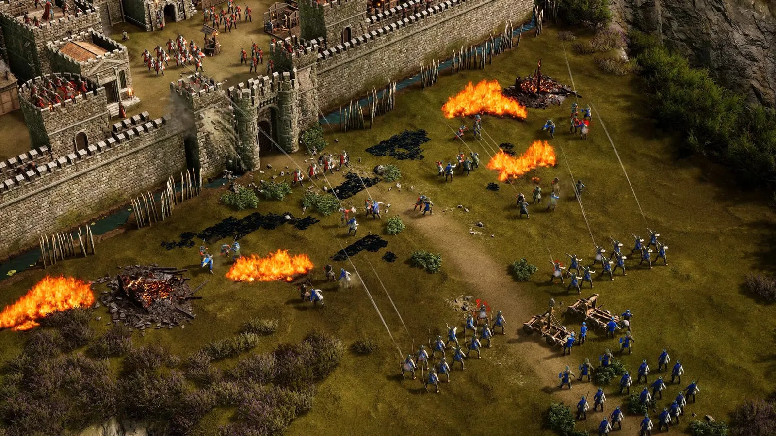 Stronghold 4 – obléhání hradu, útočníci s katapultem a hořící zbytky na bojišti
